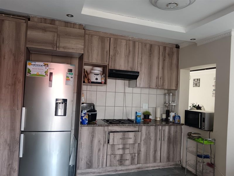 A functional kitchen featuring wood-look cabinetry, granite countertops, a gas hob with extractor fan, and tiled backsplash, with some minor ceiling plaster cracking.