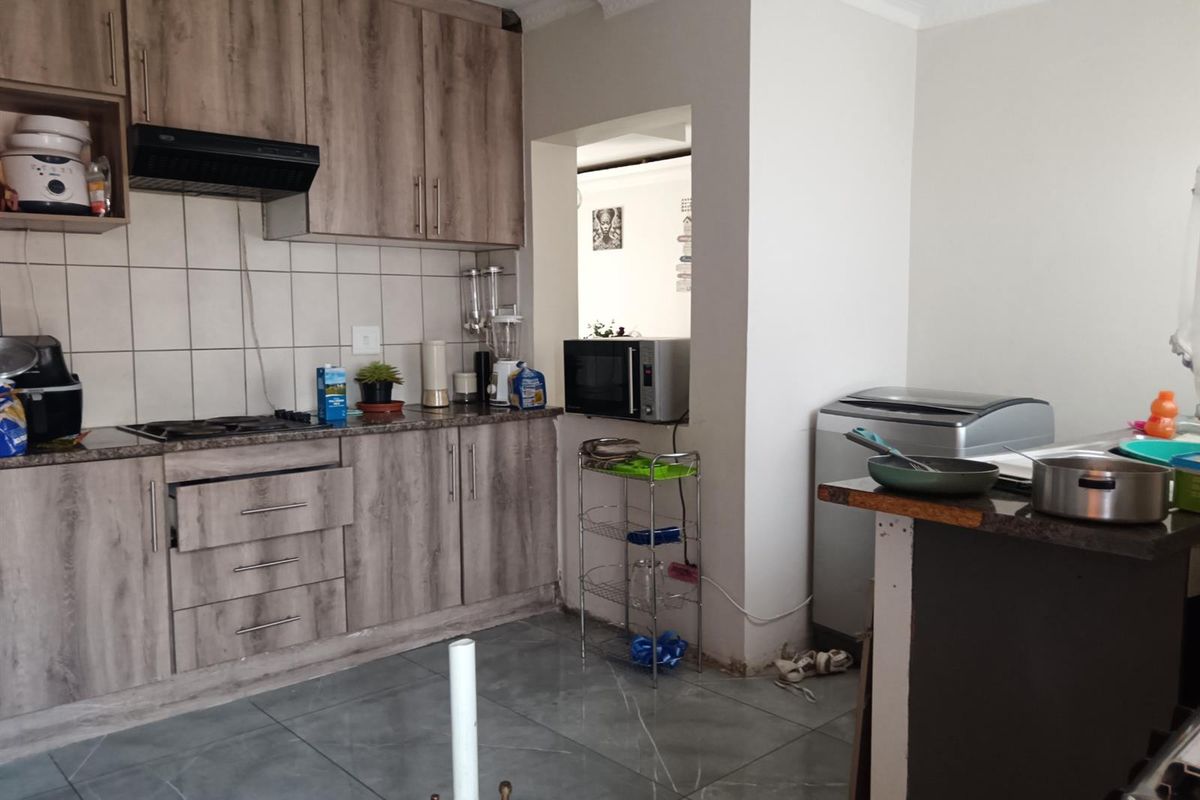 Functional kitchen featuring wood-look laminate cabinetry, granite countertops, gas hob, and tiled flooring. Requires minor finishing touches to cabinetry and flooring.