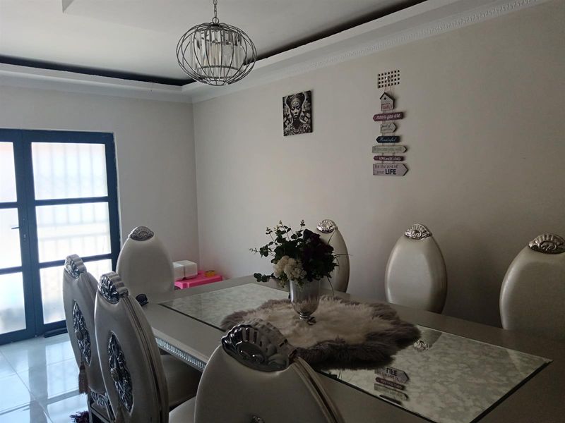 A well-maintained dining room featuring tiled flooring, decorative cove cornicing, and a modern pendant light fixture, with access to an exterior door.