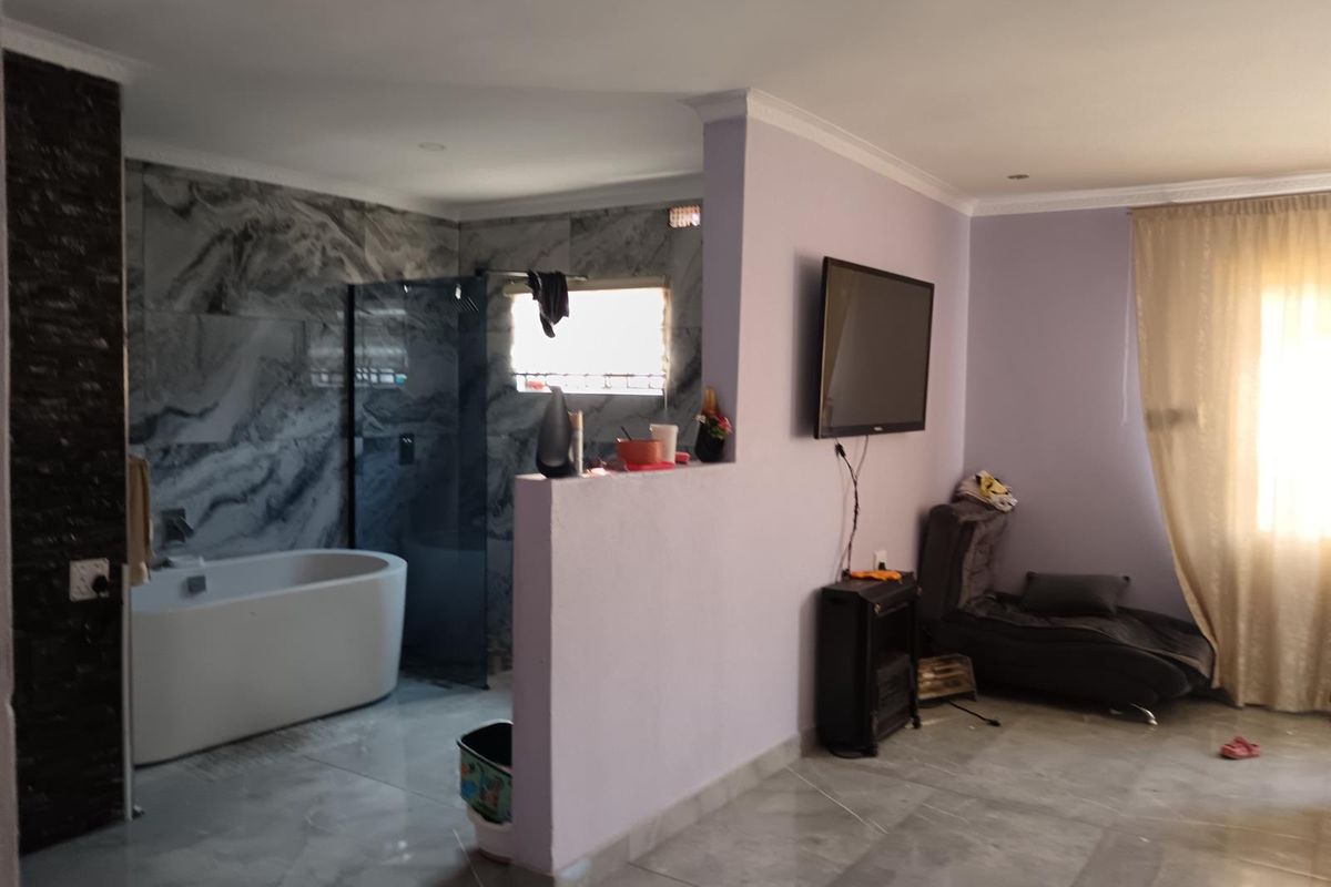 A unique open-plan bedroom suite featuring a contemporary freestanding bathtub and glass-enclosed shower area with striking marble-effect wall tiles.