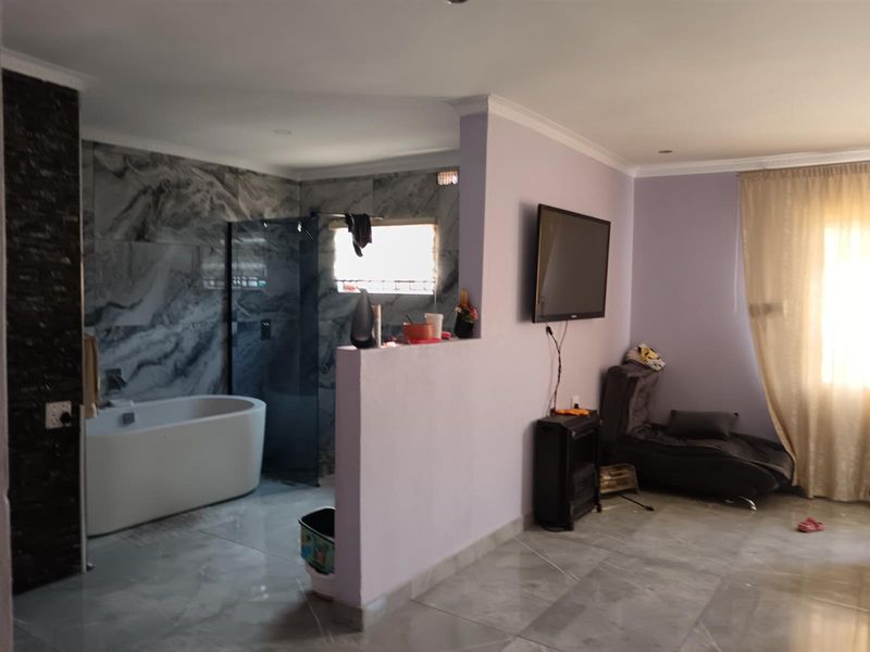 A unique open-plan bedroom suite featuring a contemporary freestanding bathtub and glass-enclosed shower area with striking marble-effect wall tiles.