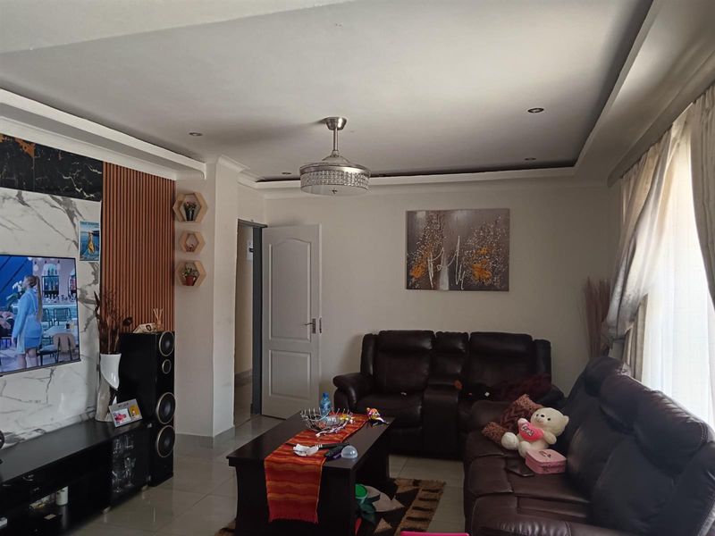 A well-maintained living room featuring a modern recessed ceiling with downlights, a ceiling fan, and a stylish combination of slatted wood and marble-effect wall paneling.