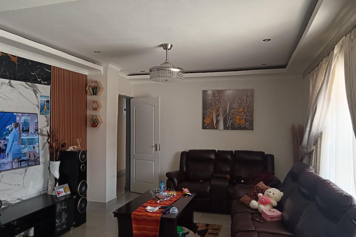 A well-maintained living room featuring a modern recessed ceiling with downlights, a ceiling fan, and a stylish combination of slatted wood and marble-effect wall paneling.
