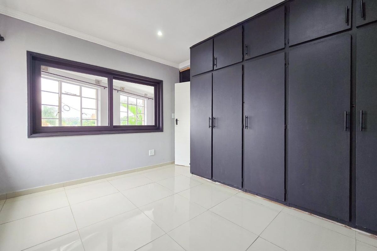 A bright, empty bedroom featuring large built-in cupboards, modern tiled flooring, and recessed downlights, offering a clean and neutral space.