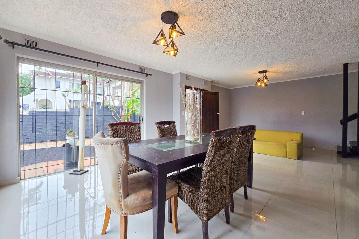 Spacious living and dining area featuring large sliding glass doors with security gates, polished tile flooring, and modern pendant lighting.