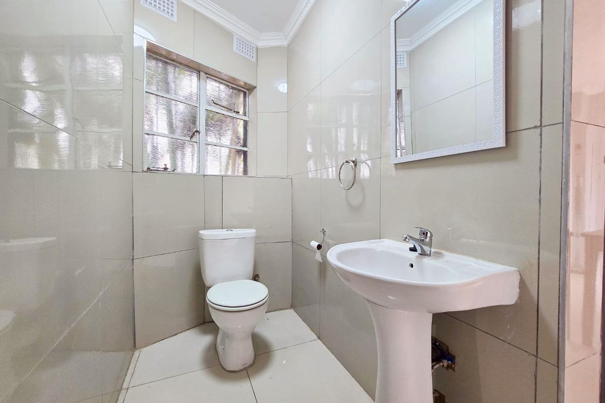 A clean, functional bathroom featuring full-height wall tiling, a pedestal basin, and a standard toilet, finished with neutral ceramic tiles.