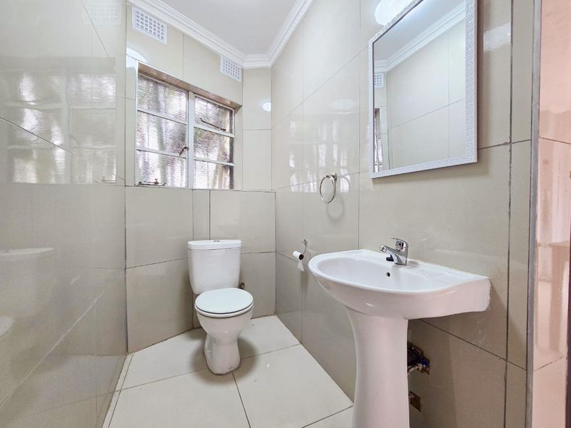 A clean, functional bathroom featuring full-height wall tiling, a pedestal basin, and a standard toilet, finished with neutral ceramic tiles.