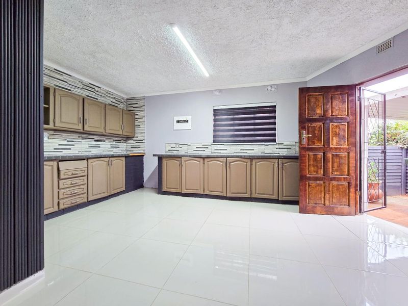 Spacious kitchen featuring extensive built-in cabinetry, tiled flooring, and a tiled backsplash, with direct access to an outdoor area through a timber door.