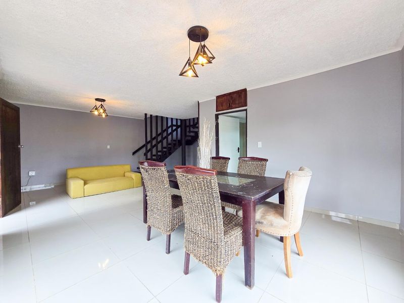 Open plan living and dining area featuring tiled flooring, modern pendant lighting, and a staircase leading to the upper level.