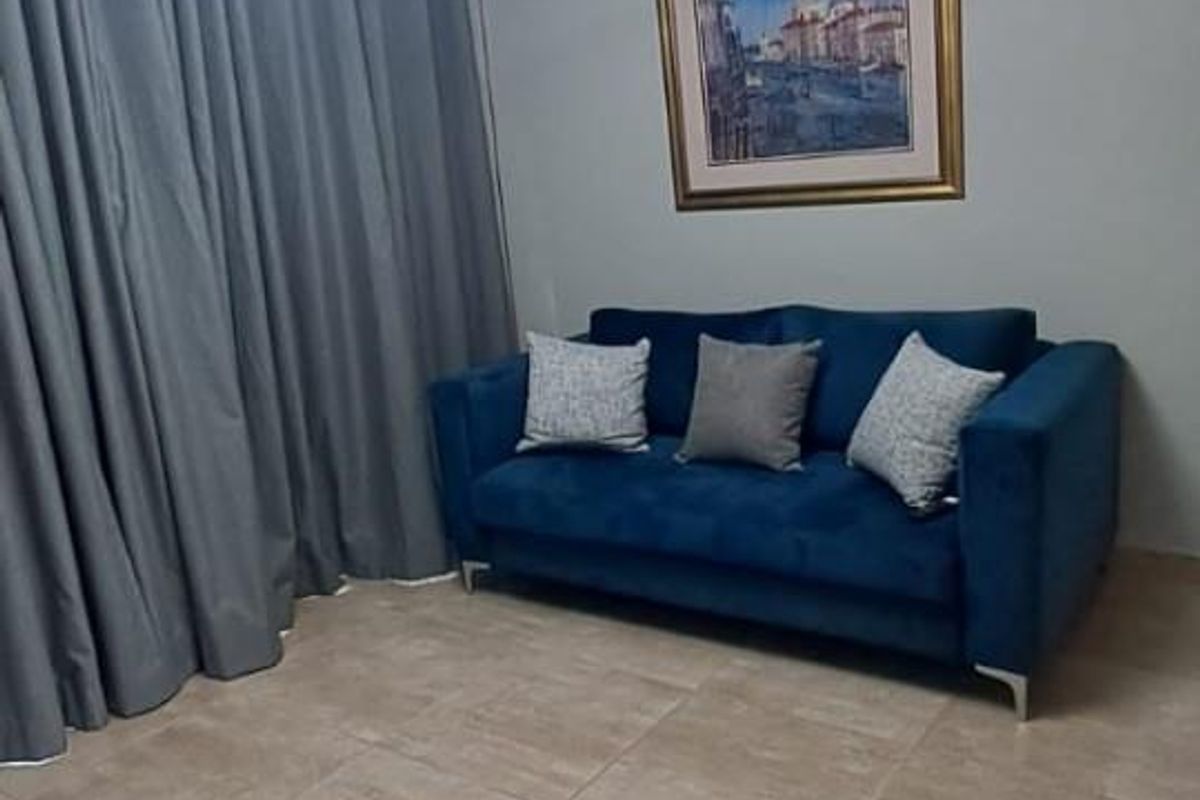 A well-maintained living room featuring neutral ceramic floor tiles, coved ceiling cornices, and a contemporary LED pendant light fixture.