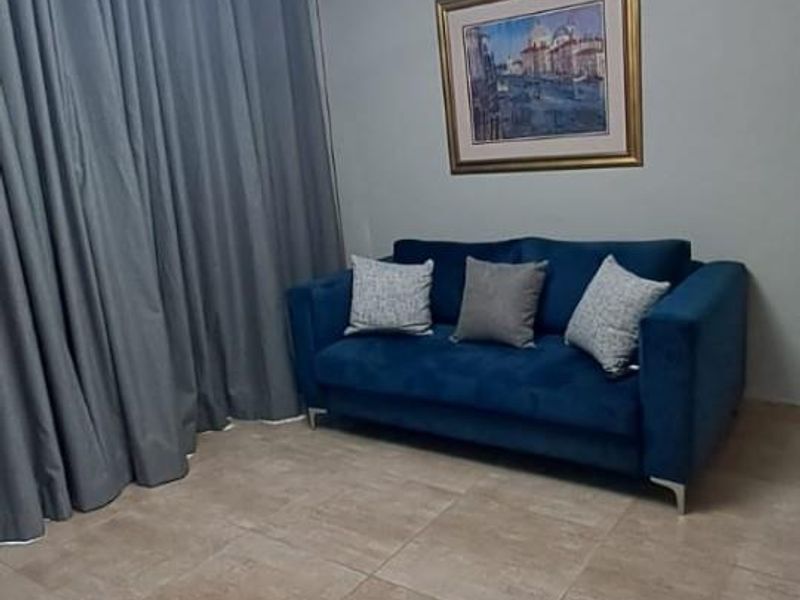 A well-maintained living room featuring neutral ceramic floor tiles, coved ceiling cornices, and a contemporary LED pendant light fixture.