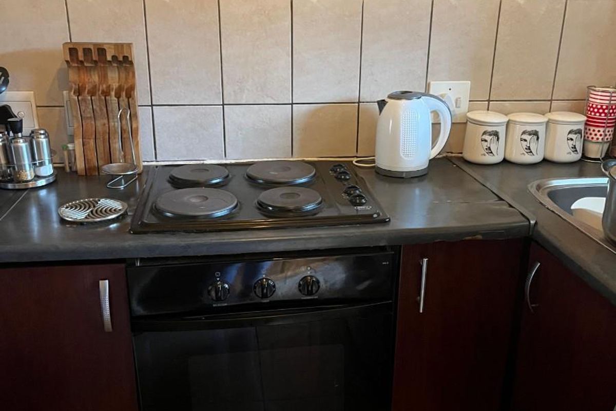 A functional kitchen area featuring a built-in oven, electric hob, tiled backsplash, and dark wood-finish cabinetry with a laminate countertop.
