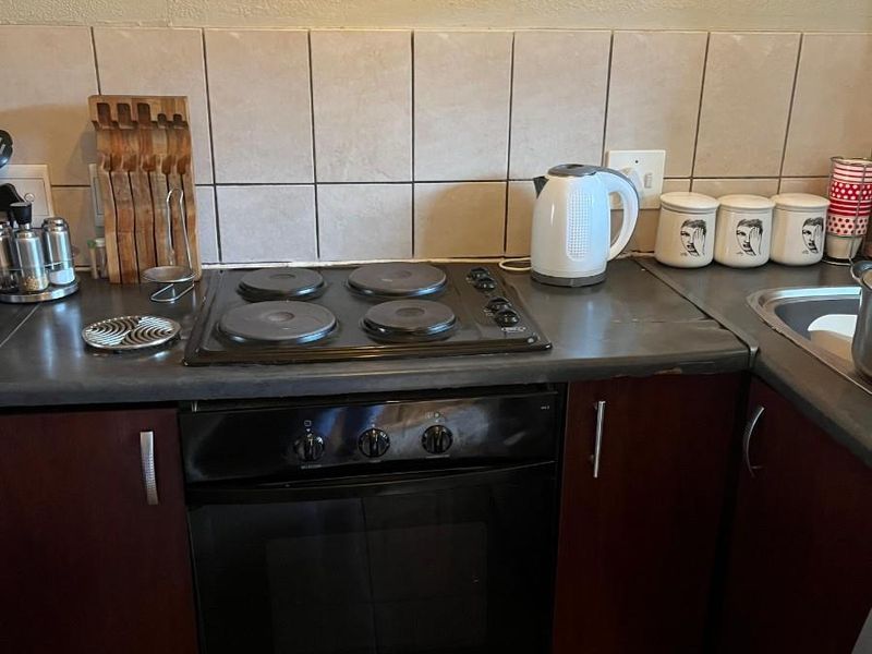 A functional kitchen area featuring a built-in oven, electric hob, tiled backsplash, and dark wood-finish cabinetry with a laminate countertop.