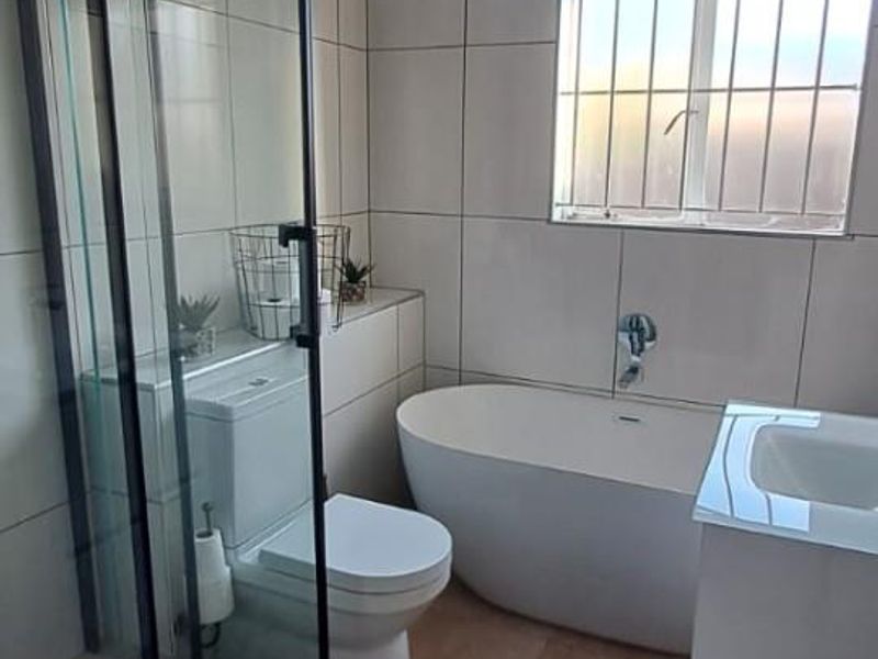 Modern bathroom featuring a freestanding bathtub, glass-enclosed shower, wall-mounted vanity, and neutral tiled finishes throughout.