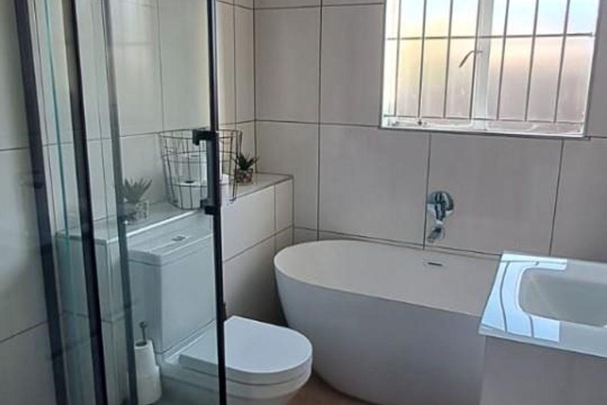 Modern bathroom featuring a freestanding bathtub, glass-enclosed shower, wall-mounted vanity, and neutral tiled finishes throughout.