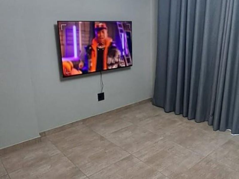 A well-maintained living room featuring neutral tiled flooring, decorative ceiling cornicing, and a modern light fixture.