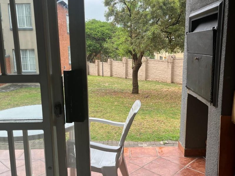 Covered patio area featuring a built-in braai, tiled flooring, and direct access to the rear garden through a sliding door.