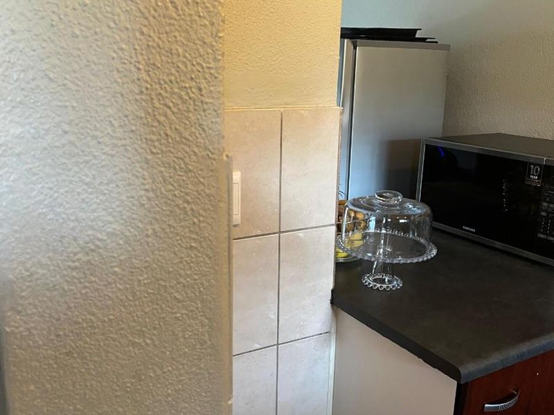 A close-up view of a kitchen corner featuring dark wood-finish cabinetry, a dark laminate countertop, and neutral tiled splashback.