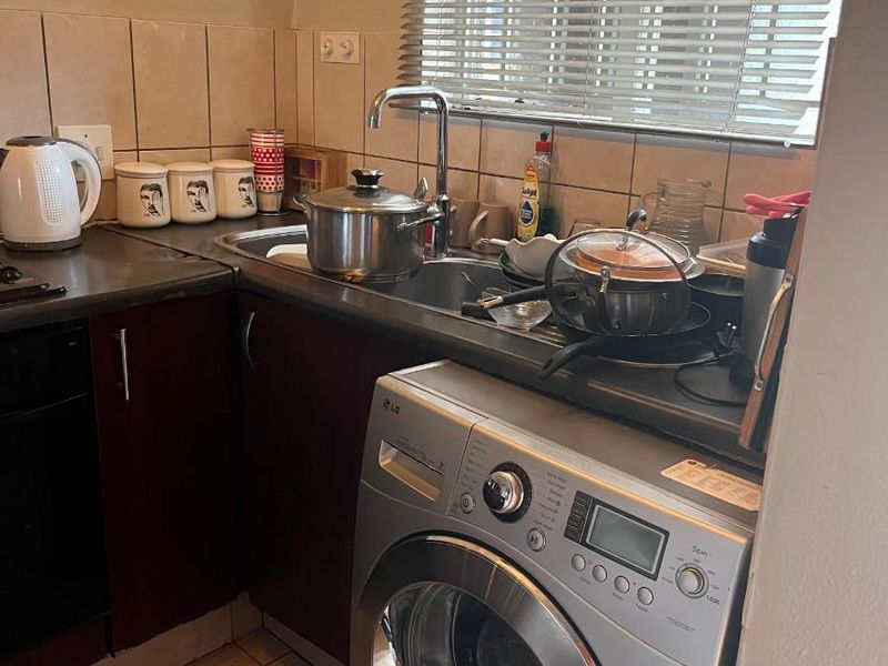 Compact kitchen area featuring dark cabinetry, laminate countertops, tiled backsplash, and a dedicated space for a front-loading washing machine.