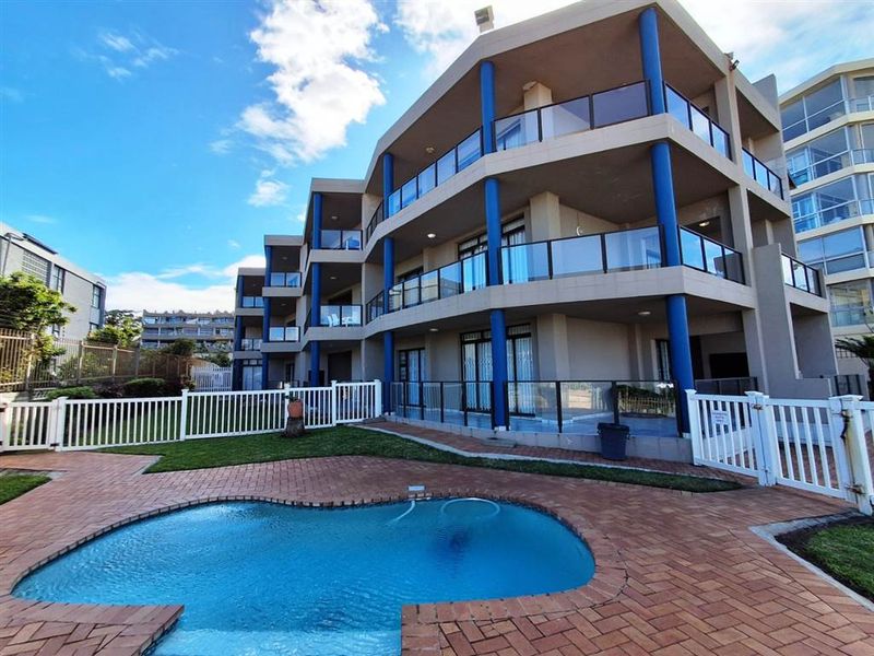 Exterior view of the apartment complex featuring a swimming pool, paved deck area, and multi-level balconies with glass balustrades.