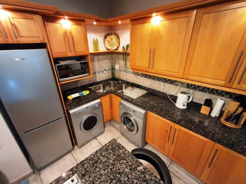 Compact kitchen featuring wooden cabinetry, granite countertops, tiled backsplash, and integrated laundry appliances.