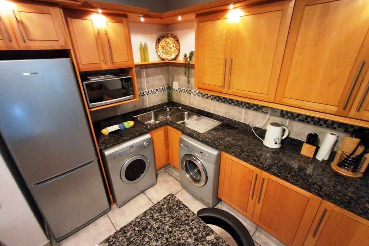 Compact kitchen featuring wooden cabinetry, granite countertops, tiled backsplash, and integrated laundry appliances.