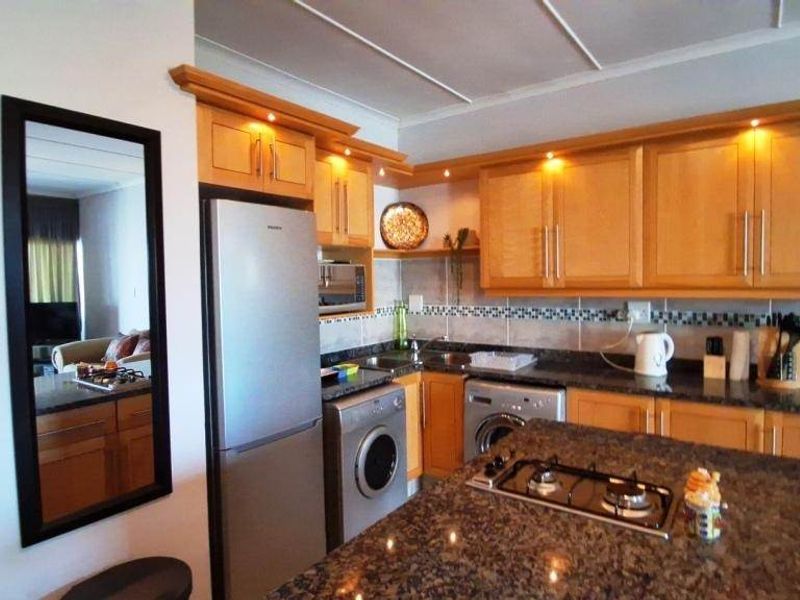 A functional kitchen featuring wooden cabinetry, granite countertops, a central island with a gas hob, and integrated appliances.