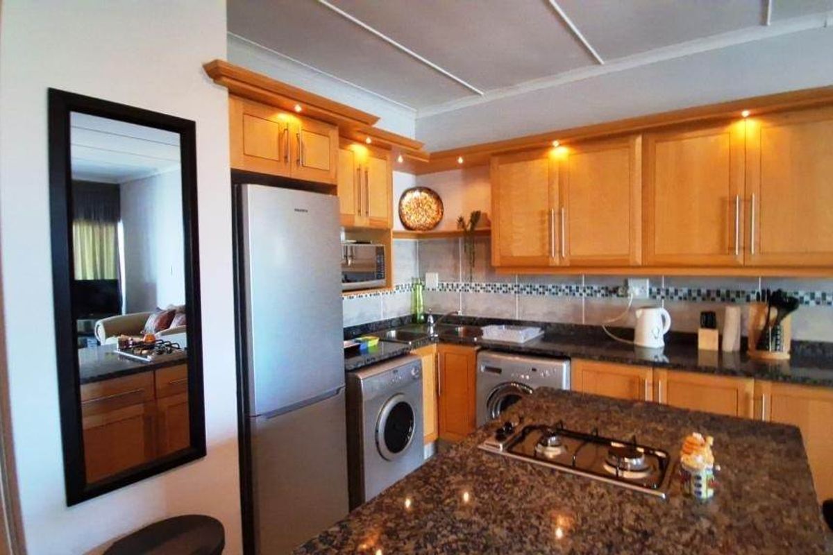 A functional kitchen featuring wooden cabinetry, granite countertops, a central island with a gas hob, and integrated appliances.