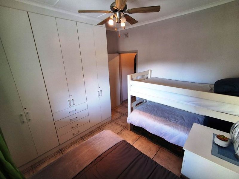 A bedroom featuring extensive built-in cupboards, tiled flooring, and a ceiling fan, providing functional storage and overhead cooling.