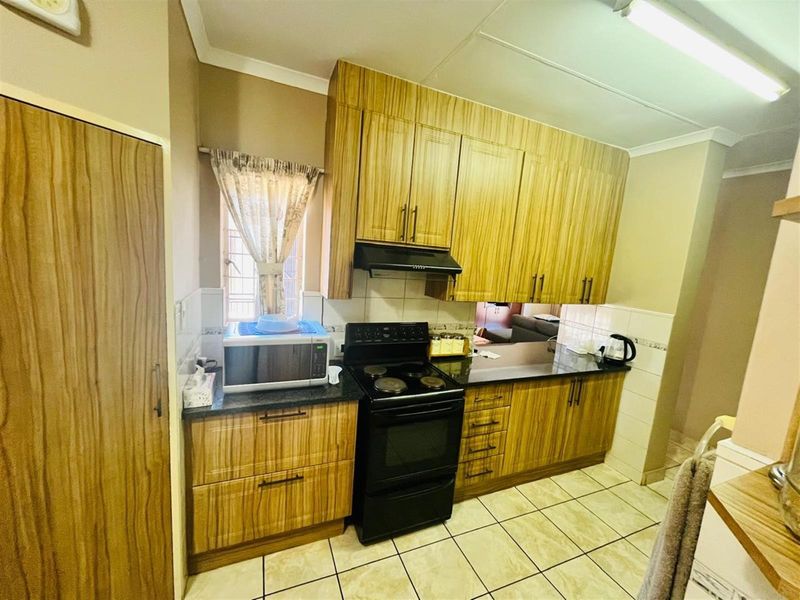 Functional kitchen featuring wood-grain cabinetry, black granite countertops, a freestanding stove with extractor fan, and tiled flooring.