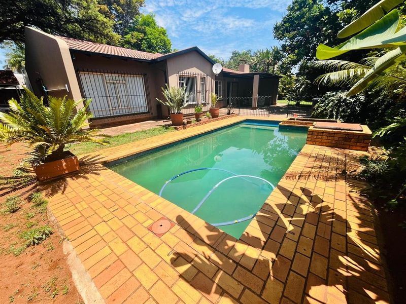 A rear exterior view featuring a swimming pool with brick paving, mature garden surroundings, and a view of the house facade.