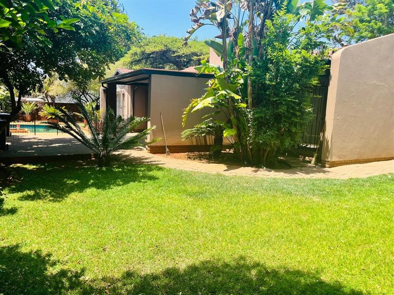A view of the rear garden featuring a paved walkway, established landscaping, and a glimpse of the swimming pool area.