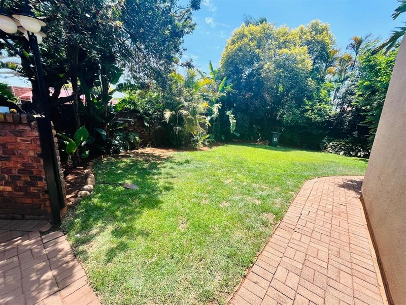 A well-maintained private garden featuring a lush lawn, mature trees, and paved walkways, providing a peaceful outdoor space.