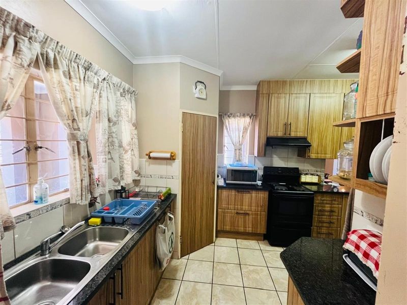 Functional kitchen featuring wood-grain cabinetry, dark granite countertops, double stainless steel sink, and a built-in extractor fan.