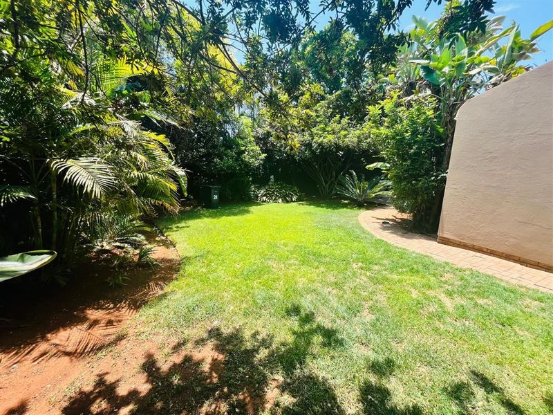 A lush, private rear garden featuring established trees, mature landscaping, and a paved walkway adjacent to the property exterior.