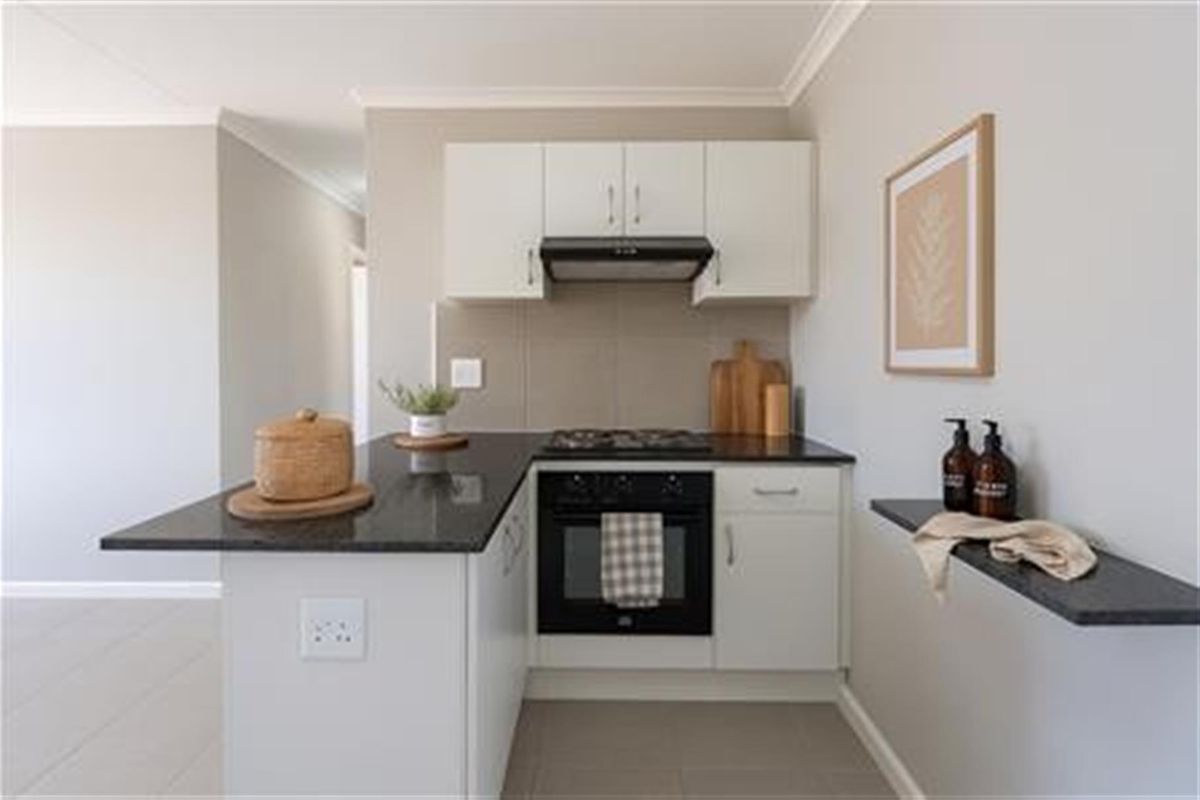 A compact, modern kitchen featuring white cabinetry, dark granite countertops, a built-in oven, gas hob, and an extractor fan.