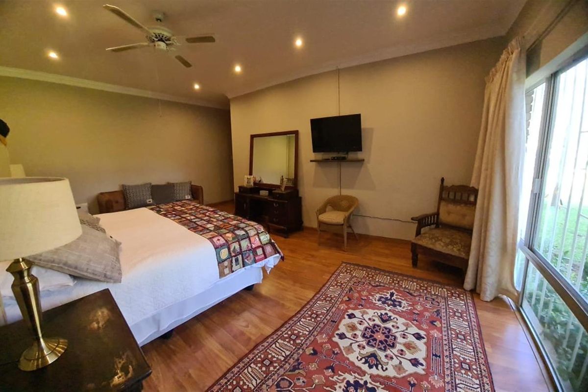 Spacious bedroom featuring warm wood-look flooring, recessed downlighting, a ceiling fan, and large sliding glass doors providing direct access to the garden.