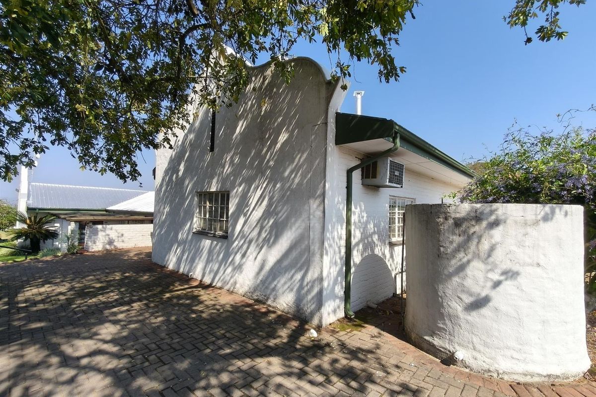 Side view of a white masonry building with a gabled roof, featuring a paved driveway, external air conditioning unit, and a cylindrical water tank.