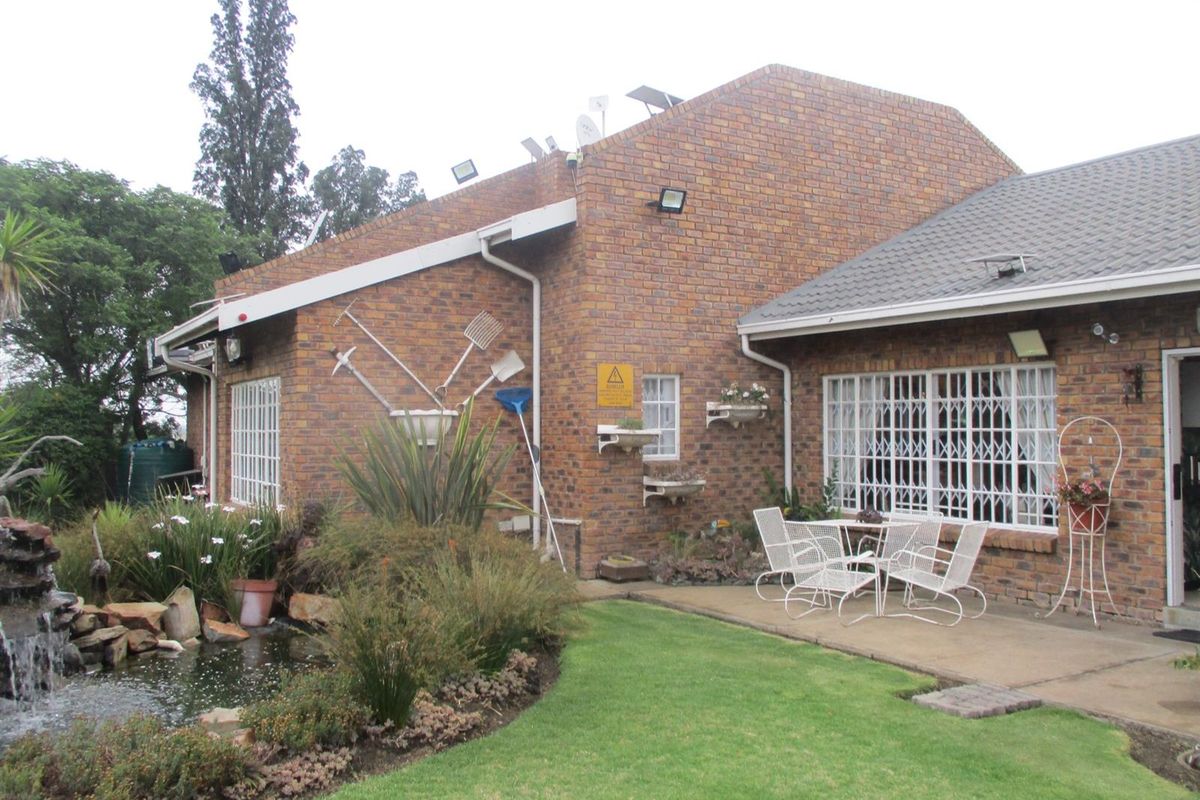 Rear exterior view of a face brick house featuring a concrete patio, landscaped garden, and a built-in water feature.