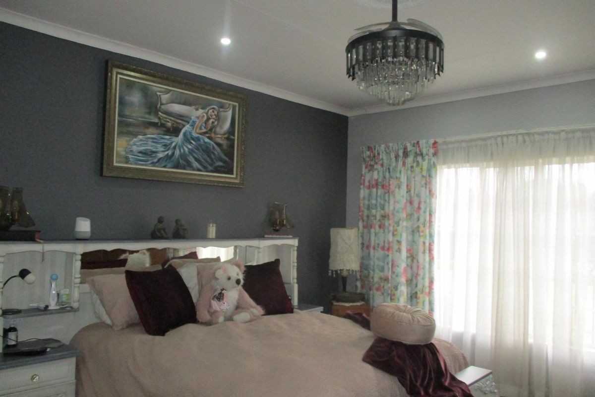 A well-maintained bedroom featuring a decorative crystal chandelier, recessed ceiling lighting, and a built-in headboard against a dark accent wall.