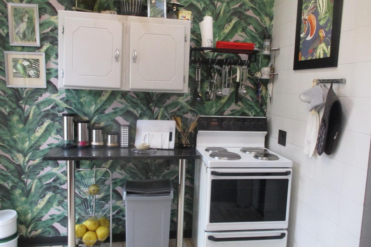 A compact kitchen area featuring a freestanding electric stove, wall-mounted cabinetry, and decorative wallpaper, providing a functional cooking space.