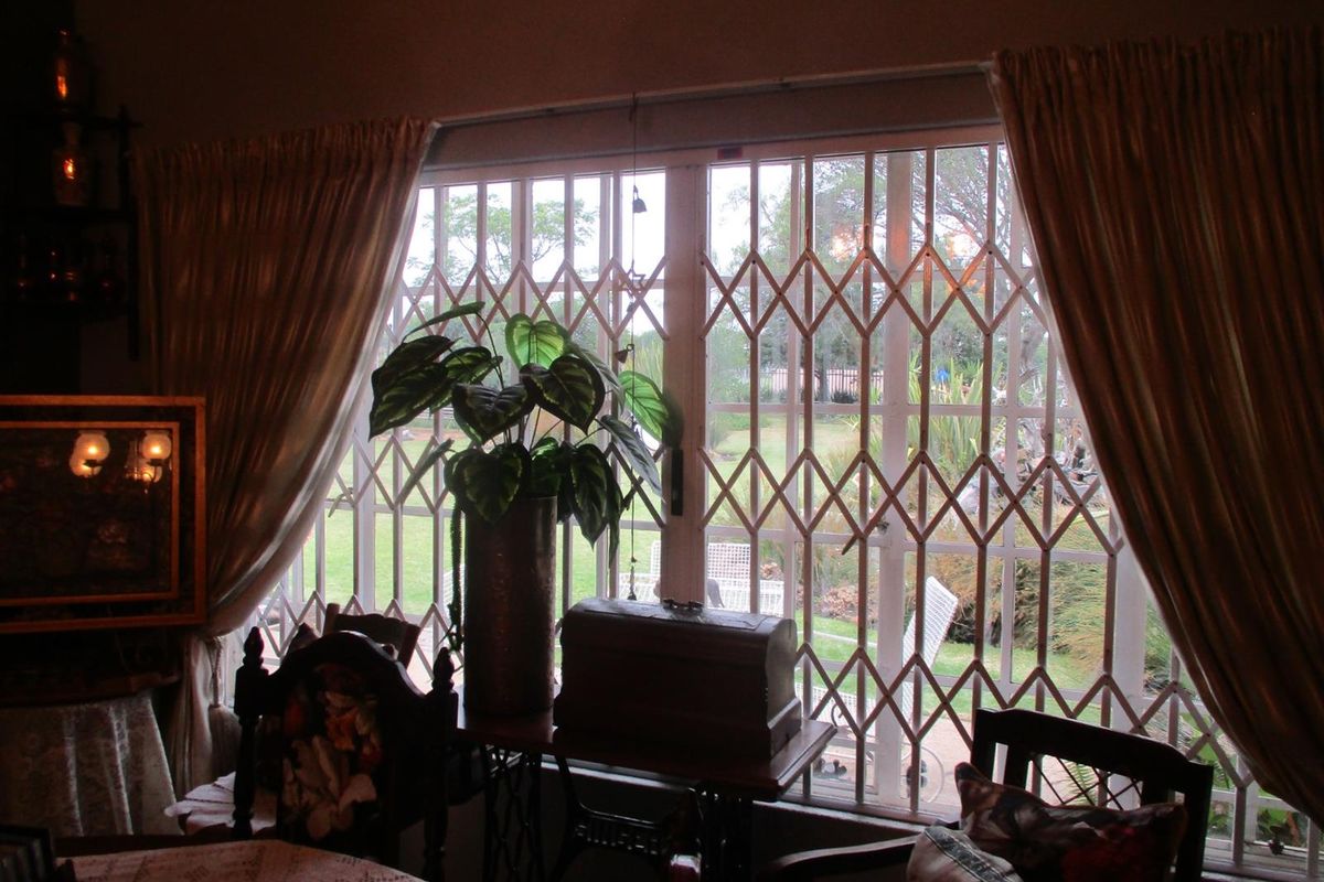 A living room area featuring a large window secured with a metal security gate, overlooking the garden.
