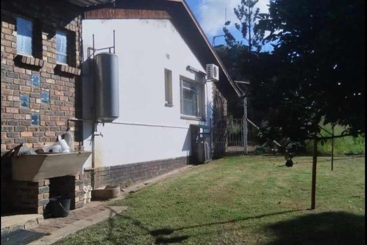 Rear exterior view of the farm property featuring a brick and plaster facade, external geyser, and a spacious garden area.