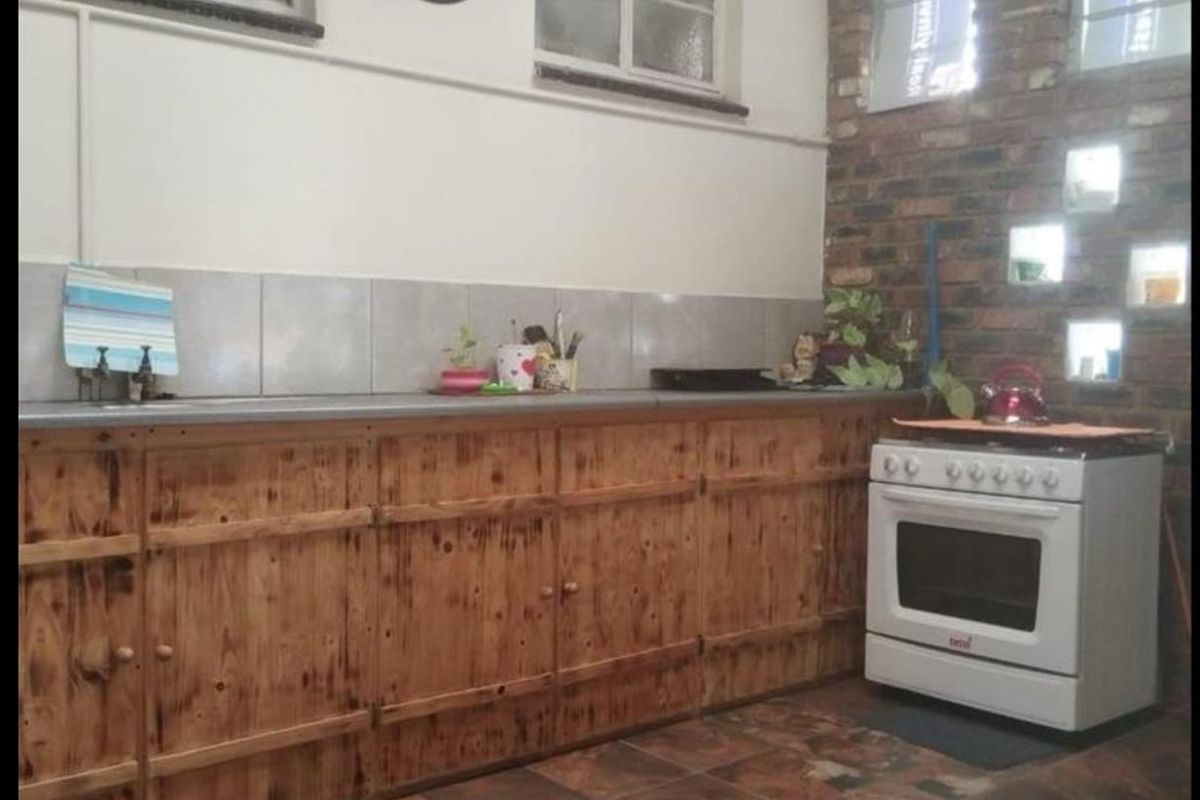 Rustic kitchen featuring wooden cabinetry, tiled backsplash, and a freestanding stove, set against a characterful exposed brick wall.