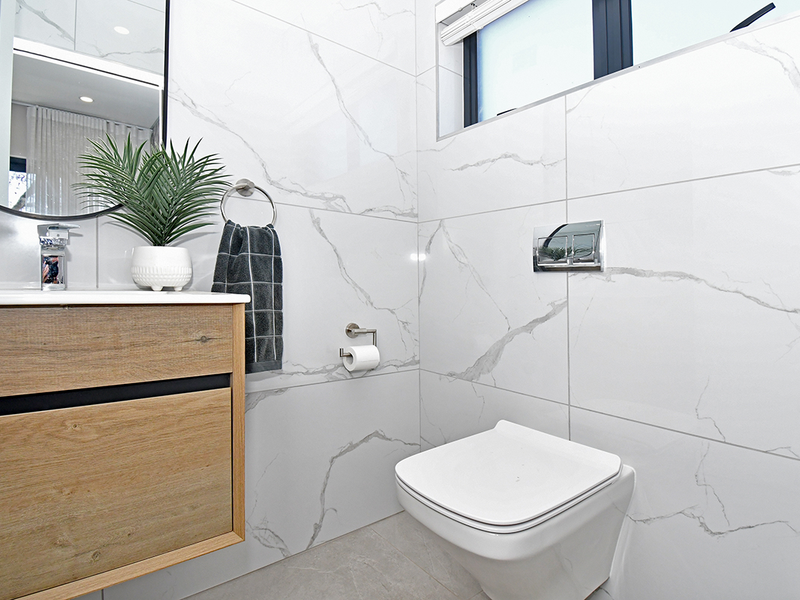 Modern bathroom featuring a floating vanity, wall-mounted toilet, and elegant marble-look porcelain wall tiles.
