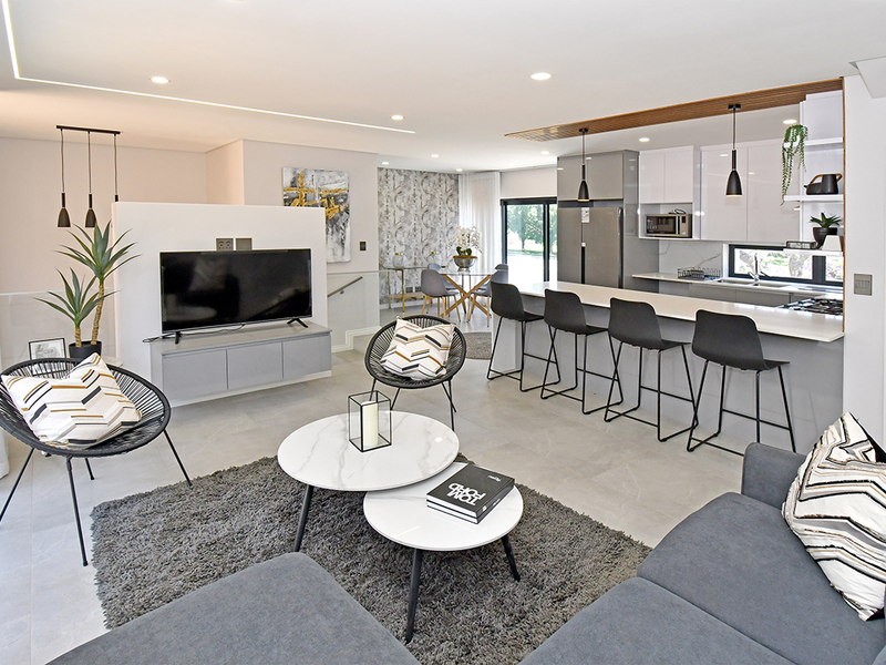 Modern open-plan living area featuring a sleek kitchen with stone countertops, a central island, and integrated appliances, seamlessly flowing into the lounge space.