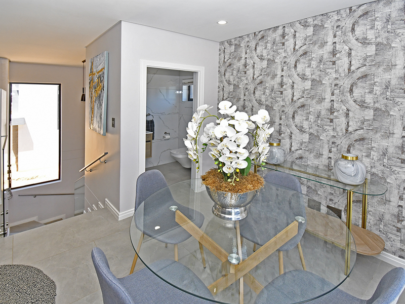 Modern dining area featuring a textured feature wall, tiled flooring, and an open-plan layout with a view into an adjacent bathroom and staircase.