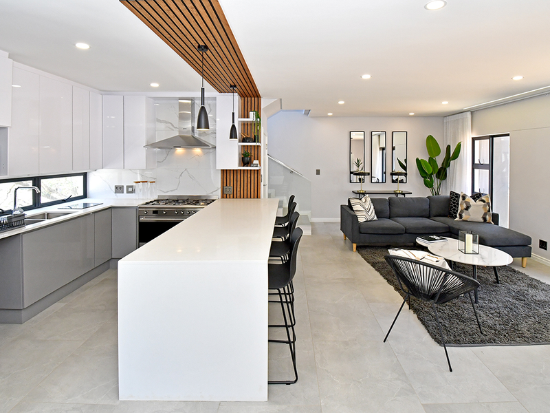 Modern open-plan living area featuring a sleek kitchen with quartz island, gas hob, and stylish timber slat ceiling detail, flowing into a comfortable lounge space.