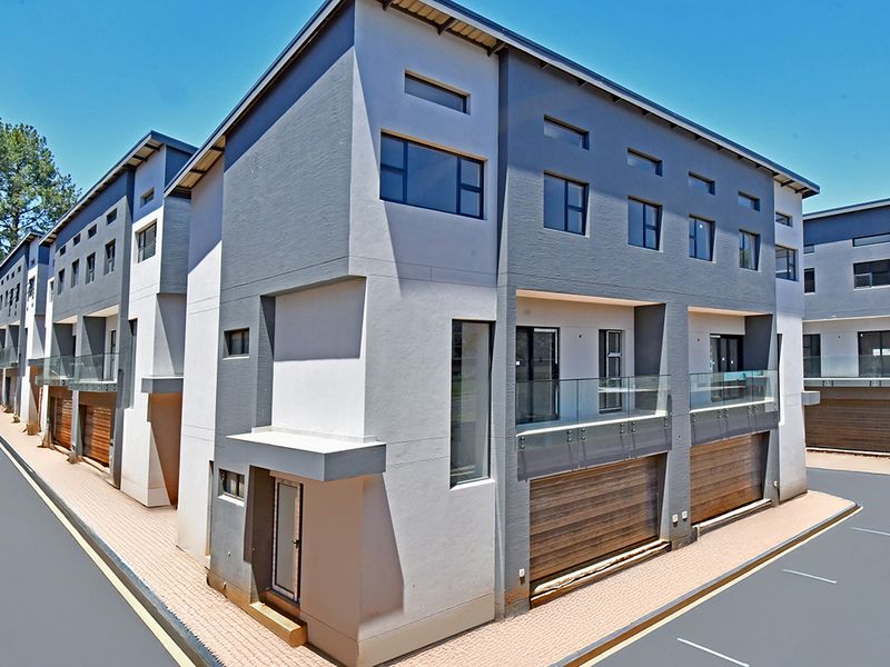 A modern multi-story residential complex featuring contemporary grey and white facade, glass balcony railings, and integrated garage access.