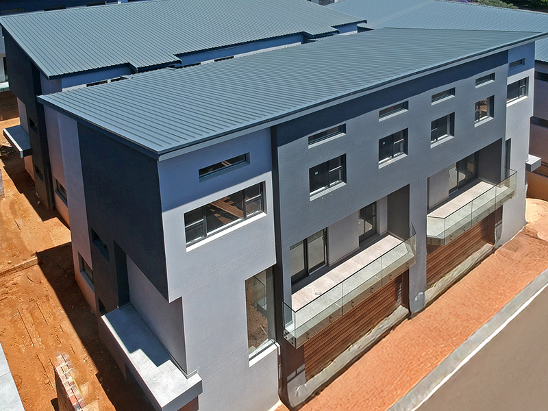Aerial view of a modern multi-story residential complex featuring contemporary architectural design, corrugated metal roofing, and glass balcony balustrades.
